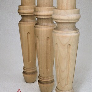 May include: Three unfinished wooden table legs with a turned design and a fluted detail. The legs are made of light-colored wood and have a smooth finish.