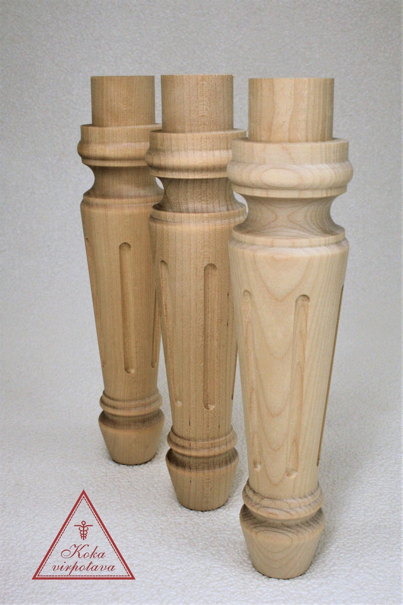 May include: Three unfinished wooden table legs with a turned design and a fluted detail. The legs are made of light-colored wood and have a smooth finish.