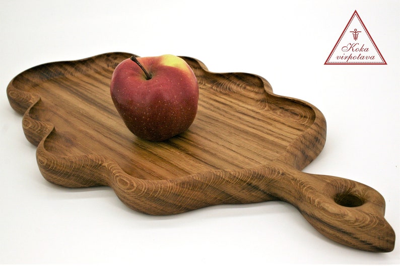 May include: A wooden serving tray with a unique cloud-like shape and a handle. The tray is made of dark wood with a natural grain pattern. An apple is sitting on the tray.