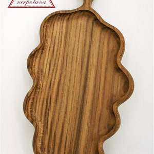 May include: A wooden serving tray with a unique, wavy edge and a handle with a hole in the top. The tray is made of dark brown wood with a natural grain pattern.