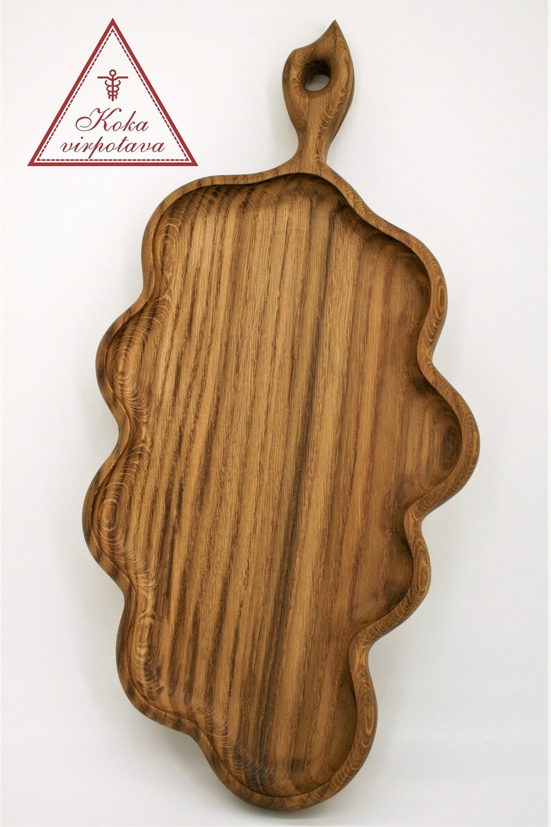 May include: A wooden serving tray with a unique, wavy edge and a handle with a hole in the top. The tray is made of dark brown wood with a natural grain pattern.