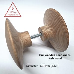May include: A pair of ash wood door knobs. The light brown knobs have a wood grain pattern. The diameter is 13 cm. The image text says "Koka virpotava" and "Pair wooden door knobs Ash wood Diameter - 130 mm (5,12")".