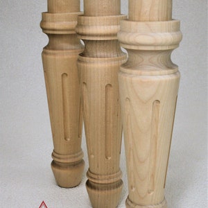 May include: Three unfinished wooden table legs with a turned design and a fluted detail. The legs are made of light-colored wood and have a smooth finish.