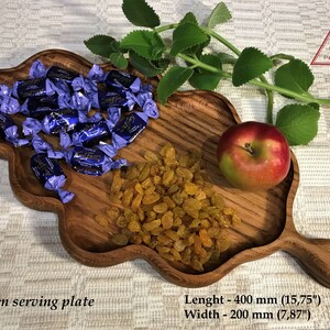 May include: Wooden serving plate with a unique, leaf-shaped design. The plate is filled with blue wrapped candies, yellow raisins, and a red apple. The plate measures 15.75 inches long and 7.87 inches wide.