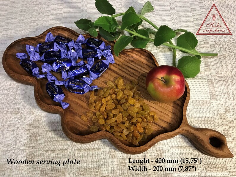 May include: Wooden serving plate with a unique, leaf-shaped design. The plate is filled with blue wrapped candies, yellow raisins, and a red apple. The plate measures 15.75 inches long and 7.87 inches wide.