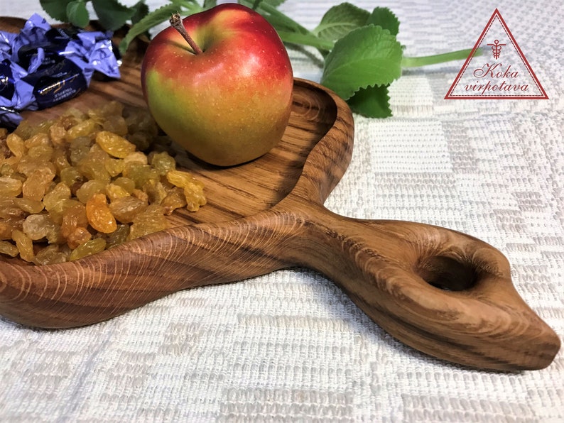 May include: A wooden serving tray with a heart-shaped bowl and a handle. The tray is filled with golden raisins and a red apple. The tray is made of natural wood and has a rustic look.