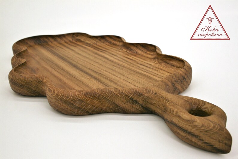 May include: A large, wooden serving tray shaped like a leaf with a handle. The tray is made of dark wood with a natural grain pattern. The handle has a hole in it for easy carrying.