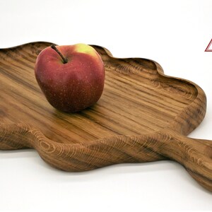 May include: A wooden serving tray with a unique cloud-like shape and a handle. The tray is made of dark wood with a natural grain pattern. An apple is sitting on the tray.