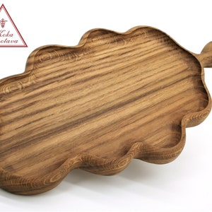 May include: A wooden serving tray shaped like an oak leaf with a handle. The tray is made of dark brown wood with a natural grain pattern.