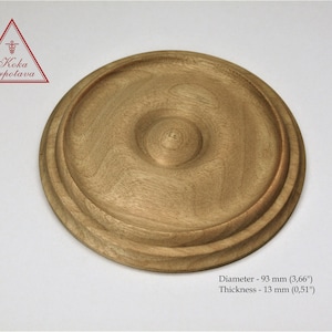 May include: A round, wooden rosette with a raised center and a diameter of 3.66 inches. The rosette is made of light brown wood and has a smooth finish.