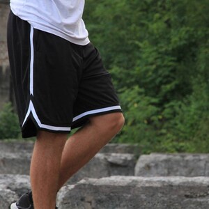 May include: Black athletic shorts with white trim along the sides and bottom hem. The shorts are made of a lightweight material and appear to be designed for sports or casual wear. The shorts are paired with a white top.