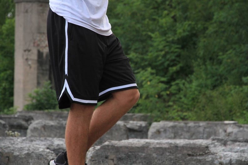 May include: Black athletic shorts with white trim along the sides and bottom hem. The shorts are made of a lightweight material and appear to be designed for sports or casual wear. The shorts are paired with a white top.