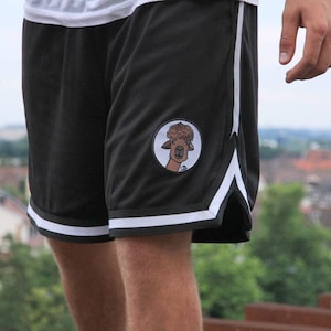 May include: Black athletic shorts with white stripes along the sides and bottom hem. A circular patch featuring a cartoon llama is on the left leg. The shorts are made of a mesh material.