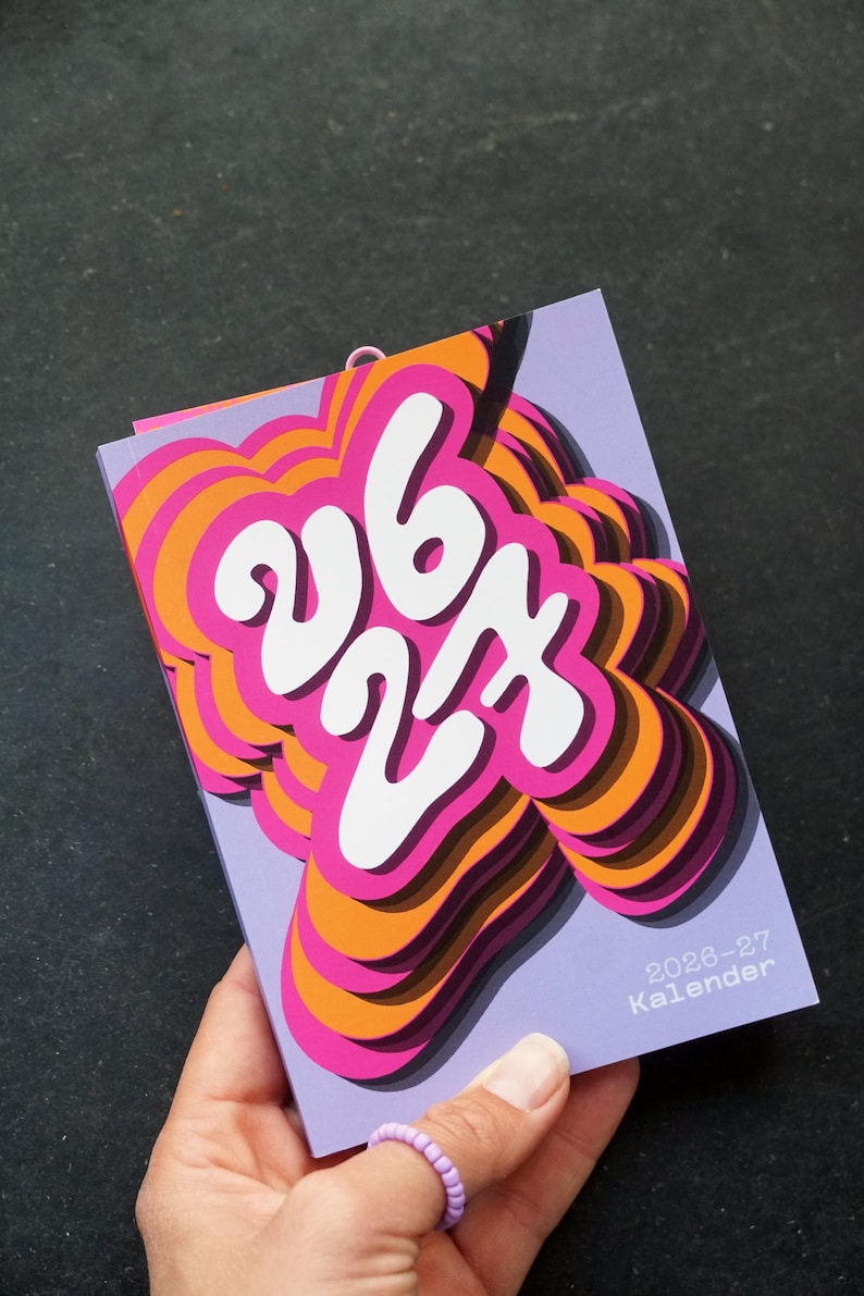 May include: A vibrant calendar with a layered design. The numbers "26 27" are in white against a pink, orange, and purple background. The text "2026-27 Kalender" is visible. The calendar is held in a hand.