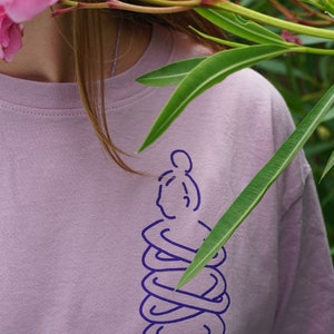 May include: A light purple t-shirt with a purple outline of a person sitting in a meditative pose.