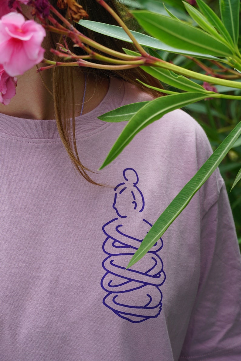 May include: A light purple t-shirt with a purple outline of a person sitting in a meditative pose.