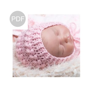 May include: A pink crocheted baby bonnet with a gathered top and a tie at the back.