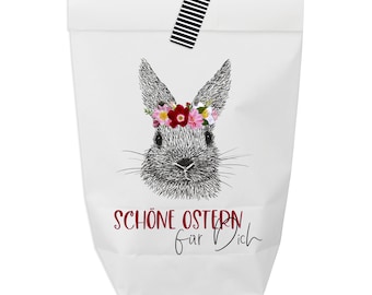 May include: White gift bag with a black and white striped handle. The bag features a black and white illustration of a bunny wearing a pink and red flower crown. The text "Schöne Ostern für Dich" is printed in red on the bag.
