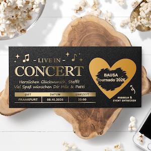 Könnte beinhalten: Ein schwarzes Konzertticket mit goldfarbenen Buchstaben und Akzenten. Auf dem Ticket steht "LIVE IN CONCERT" und enthält Datum, Uhrzeit und Ort. Eine goldene Herzform mit dem Text "BAUSA Tournado 2026" befindet sich auf der rechten Seite.