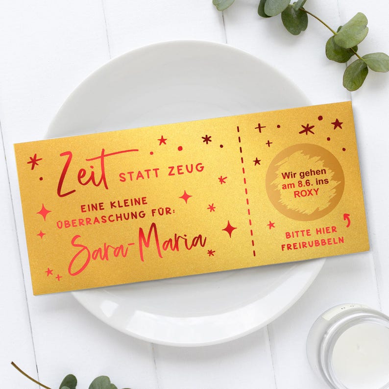 May include: A gold-colored gift certificate with red text and star accents. The text includes "Zeit statt Zeug" and "Sara-Maria". A scratch-off area reveals "Wir gehen am 8.6. ins ROXY".