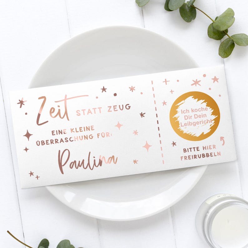 May include: A white gift certificate with rose gold text and star accents, resting on a white plate. The text includes "Zeit statt Zeug" and "Paulina". A gold circle with German text is on the right side.
