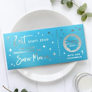 May include: A teal gift certificate with silver text and star accents. The text reads "Zeit statt Zeug" and "Eine kleine &Uuml;berraschung f&uuml;r: Sara-Maria". A scratch-off area says "Wir gehen am 8.8 ins ROXY".