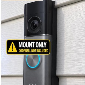 May include: A black and grey video doorbell mount with a rectangular shape. The device features a camera lens at the top and a circular button with a blue light ring. Text on the image reads: MOUNT ONLY DOORBELL NOT INCLUDED.
