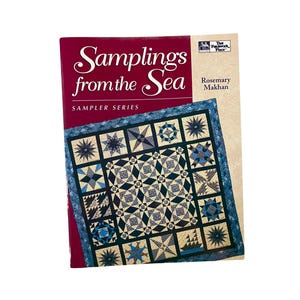 May include: A softcover book titled Samplings from the Sea by Rosemary Makhan, part of the Sampler Series. The cover features a blue and white quilt with various star and nautical patterns, set against a deep red and cream background.