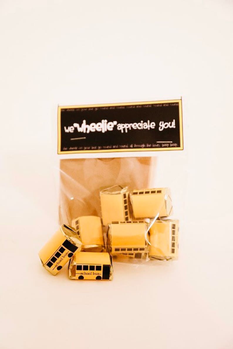 May include: A clear plastic bag filled with small yellow and black school bus-shaped chocolates. The bag has a black and white tag that reads "we wheelie' appreciate you!"