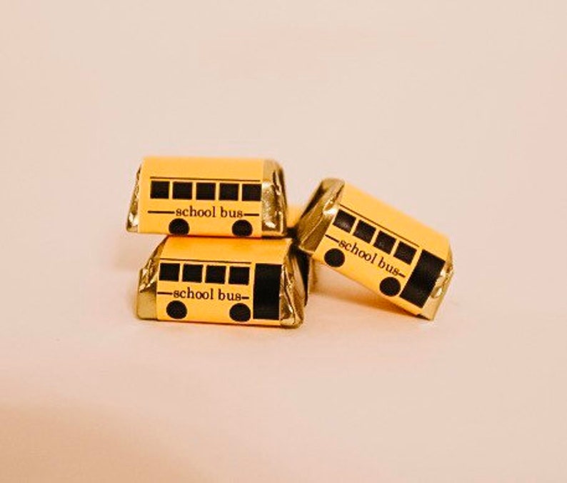 May include: Three small chocolate bars wrapped in yellow paper with black school bus designs and the text "school bus" printed on each bar.