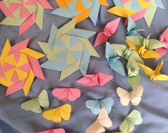 May include: A collection of colorful origami paper crafts, including butterflies, stars, and flowers. The crafts are arranged on a light blue fabric background.