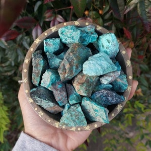 A tribal marked bowl sitting in a palm full of rough chunks of vibrant blue stones.