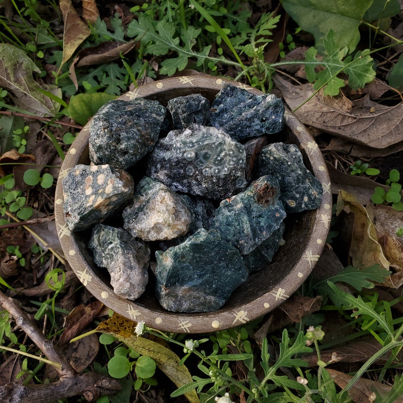 A tribal marked bowl sitting in a patch of grass full of deep green stones with orbicular patterns.
