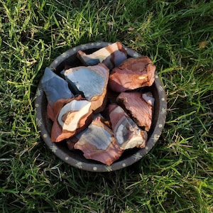May include: A bowl filled with colourful, natural, polished stones. The stones have a variety of patterns and colours, including red, brown, white, and grey. The bowl is made of wood and has a decorative pattern.
