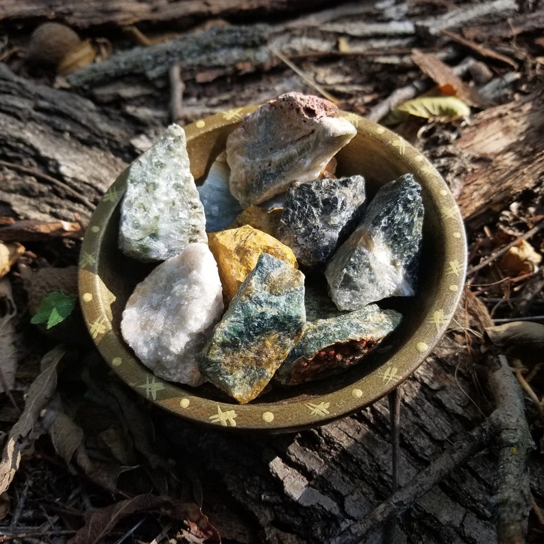 A tribal marked bowl sitting in a patch of grass full of deep green, brown, and yellow stones with orbicular patterns.