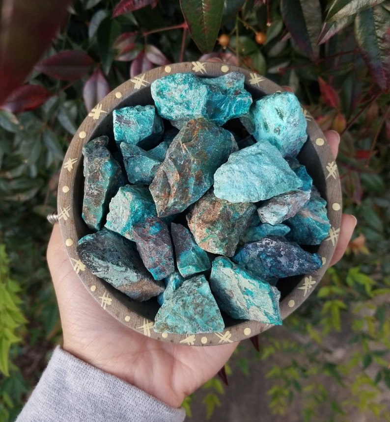 A tribal marked bowl sitting in a palm full of rough chunks of vibrant blue stones.