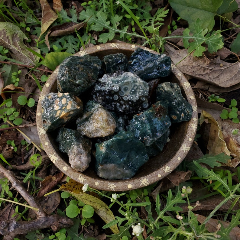 A tribal marked bowl sitting in a patch of grass full of deep green stones with orbicular patterns.