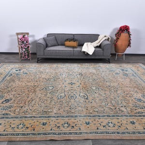 Op de afbeelding: Een groot, beige vloerkleed met een blauw en cr&egrave;mekleurig bloemenpatroon. Het vloerkleed heeft een gedetailleerde rand met een herhalend patroon.