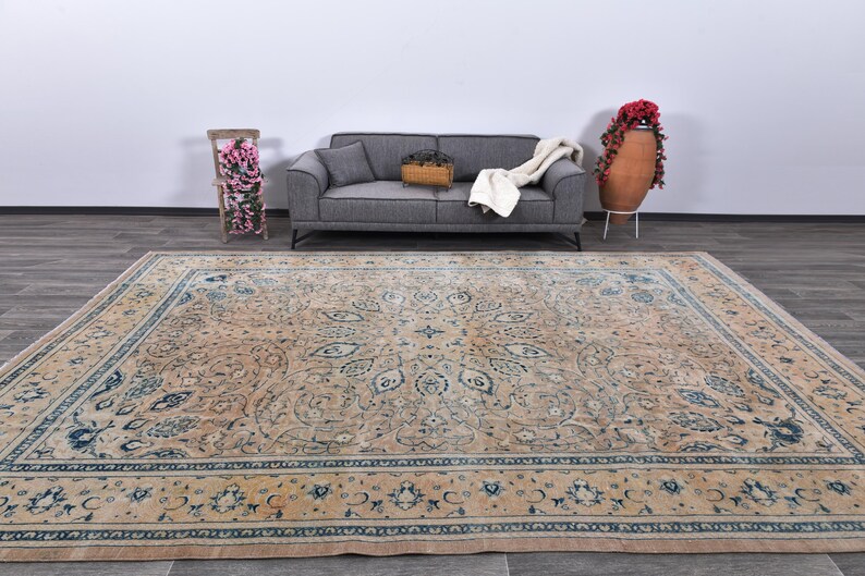 Op de afbeelding: Een groot, beige vloerkleed met een blauw en cr&egrave;mekleurig bloemenpatroon. Het vloerkleed heeft een gedetailleerde rand met een herhalend patroon.