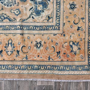 Op de afbeelding: Een vintage tapijt met een beige achtergrond en een blauw en wit bloemenpatroon. Het tapijt heeft een franje rand.