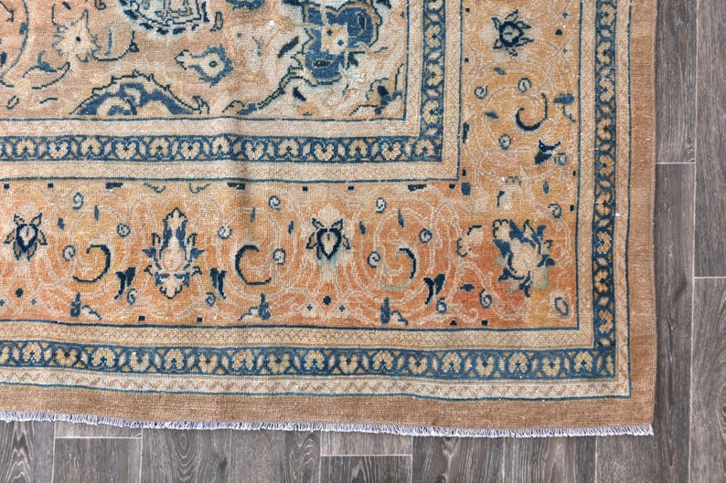 Op de afbeelding: Een vintage tapijt met een beige achtergrond en een blauw en wit bloemenpatroon. Het tapijt heeft een franje rand.