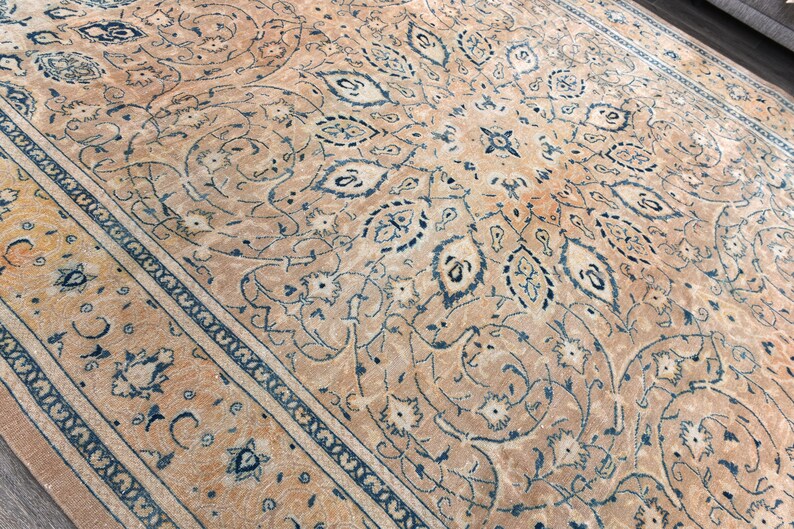 Op de afbeelding: Een beige kleed met een blauw en wit bloemenpatroon. Het kleed heeft een rand met een herhalend patroon.