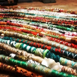 Op de afbeelding: Een close-up van een verscheidenheid aan kleurrijke garenstrengen, sommige met kralen, gerangschikt in rijen. De strengen zijn gemaakt van verschillende texturen en patronen, waardoor een visueel aantrekkelijke en textuurrijke weergave ontstaat.