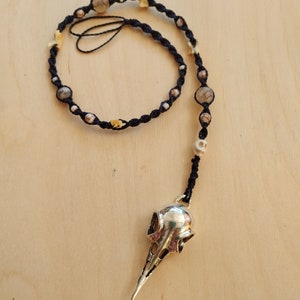 May include: A black cord necklace with agate beads, bone beads, and a silver bird skull pendant.