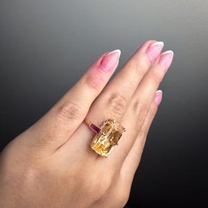 Peut inclure: Une bague en or ornée d'une grande pierre jaune rectangulaire à facettes montée sur griffes. L'anneau présente un accent en pierre rose foncé rectangulaire plus petit, positionné horizontalement à côté de la pierre jaune principale.