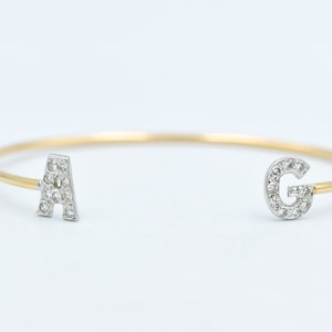 May include: A gold bangle bracelet with two letters, A and G, set with diamonds.