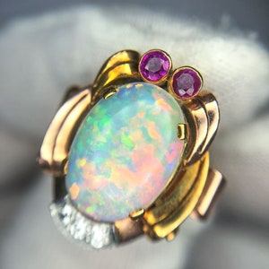 May include: A gold ring with an oval opal gemstone and two small pink gemstones. The ring has a delicate design with intricate details.