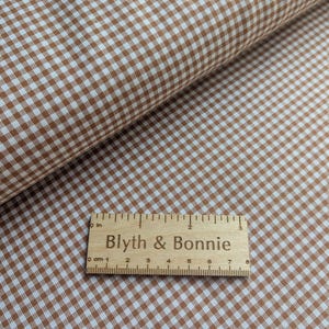 May include: Brown and white gingham fabric with a wooden ruler that reads "Blyth & Bonnie". The fabric is folded over, showing the pattern in detail. The ruler is marked in centimetres.