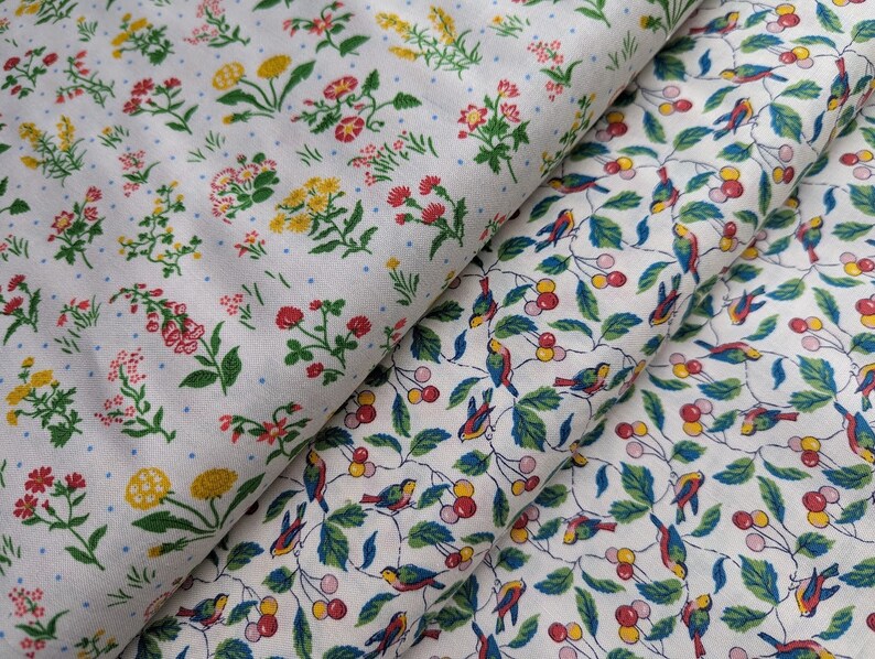 Pode incluir: Duas amostras de tecido com padr&otilde;es diferentes. A amostra superior tem um fundo branco com um padr&atilde;o repetitivo de pequenas flores vermelhas, amarelas e verdes. A amostra inferior tem um fundo branco com um padr&atilde;o repetitivo de p&aacute;ssaros azuis e bagas vermelhas em galhos verdes.