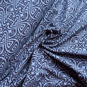 Könnte beinhalten: Nahaufnahme eines Stoffes mit einem sich wiederholenden geometrischen Muster in Blau- und Dunkelgrautönen. Das Design zeigt ineinandergreifende Formen und Linien, die ein strukturiertes Aussehen erzeugen. Der Stoff ist drapiert und zeigt Falten und Schatten, die dem Muster Tiefe verleihen.